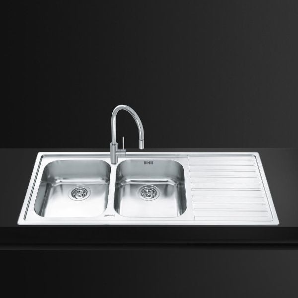 Stainless steel double bowl kitchen sink with faucet and drainboard on dark background