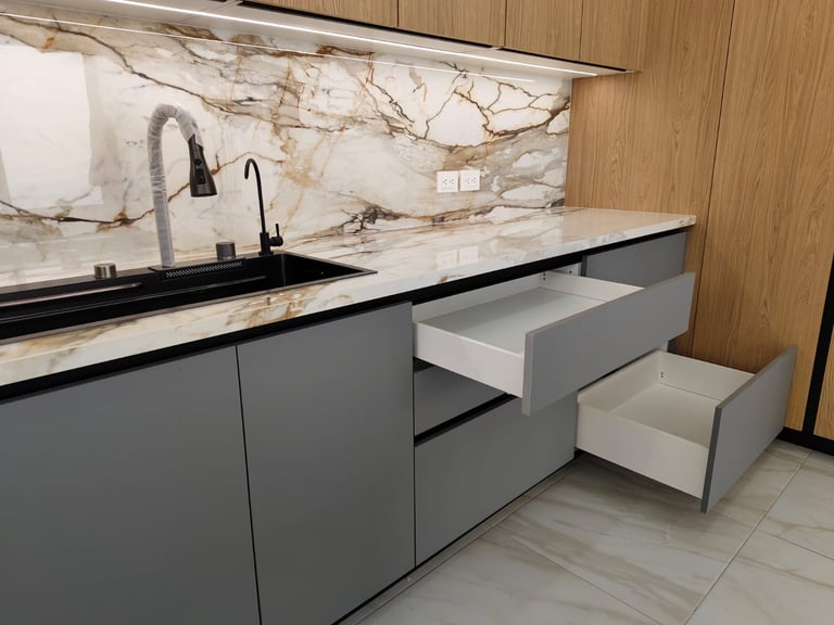 Modern kitchen with gray cabinets, marble backsplash, black sink, and pull-out drawers on a light tile floor