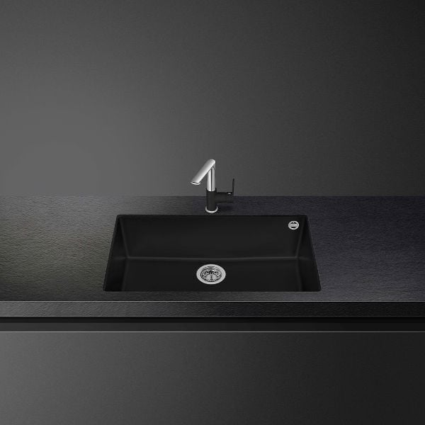 Modern black kitchen sink with faucet mounted on gray countertop against dark background