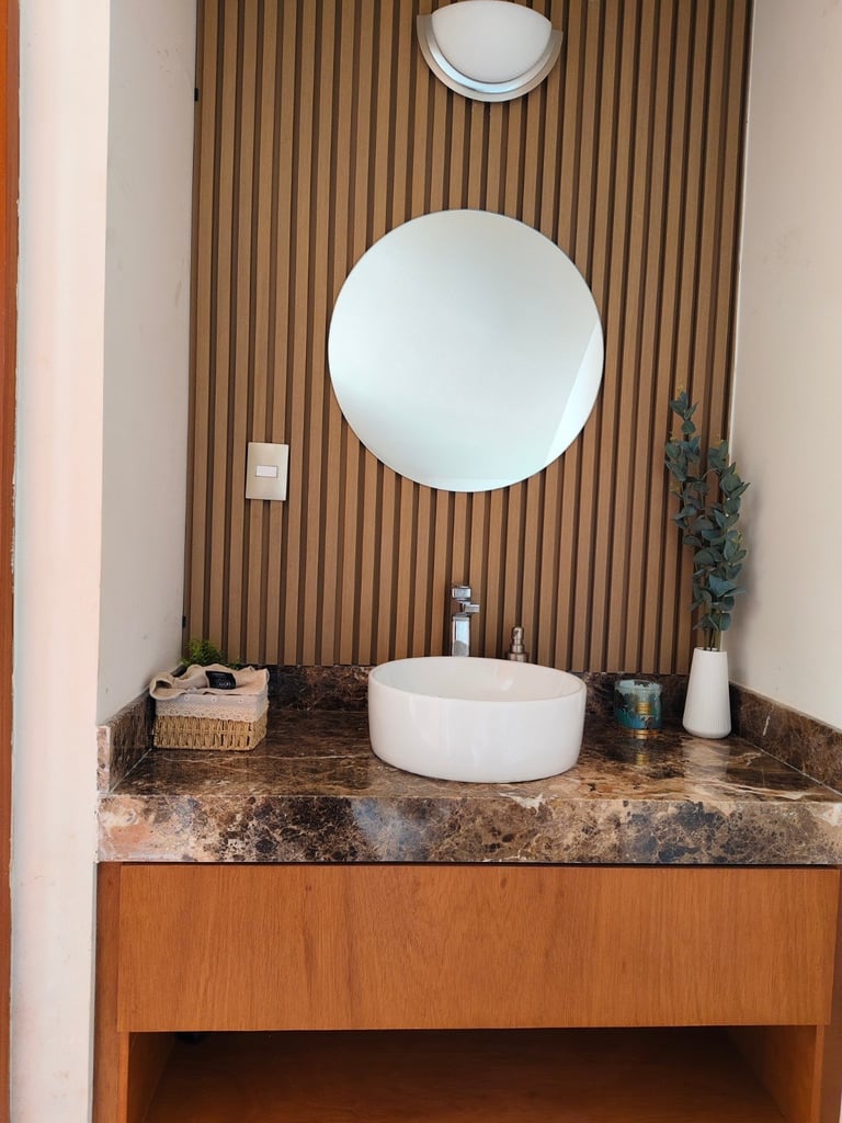 Modern bathroom vanity with round white ceramic sink, marble countertop, wood paneled wall, and two circular mirrors