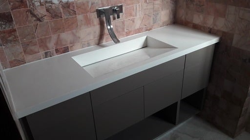 Modern bathroom vanity with white countertop, integrated sink, and black cabinet base against red tile wall