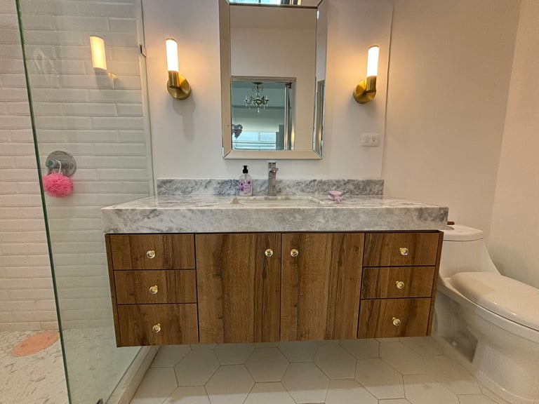 Modern bathroom vanity with wood cabinets, marble countertop, mirror, and wall sconces above sink